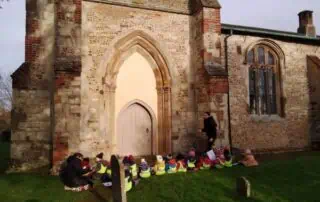 Children sitting outside a historic church during an outdoor educational activity at Monkey Puzzle Day Nurseries.