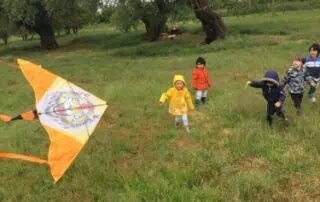Colorful children flying a kite outdoors during daytime at Monkey Puzzle Day Nurseries, promoting outdoor play and children's activities.