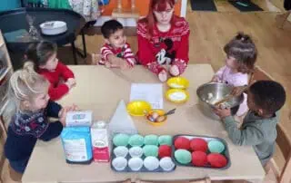 Colorful preschool classroom with children engaging in baking activity under supervision at Monkey Puzzle Day Nurseries.