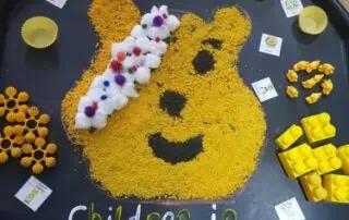 Colorful sensory activity tray featuring rice, small toys, and craft materials for children at Monkey Puzzle Day Nurseries, promoting early childhood development and learning.