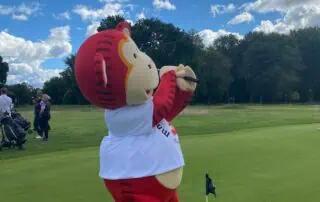 Colorful mascot in sports attire on golf course promoting fun activities at Monkey Puzzle Day Nurseries.