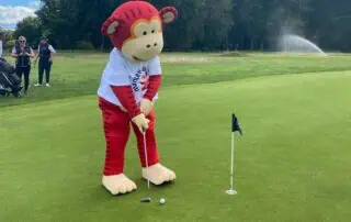 Colorful monkey mascot playing mini-golf on the lush green course at Monkey Puzzle Day Nurseries outdoor activity day.