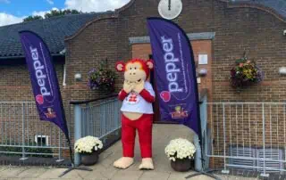 Colorful monkey mascot outside Monkey Puzzle Day Nurseries, with flags and flowers, welcoming children.
