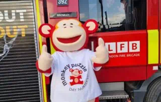 Bright red fire truck with firefighter and a person in a monkey puzzle daycare mascot costume, promoting safety and community events at Monkey Puzzle Day Nurseries.