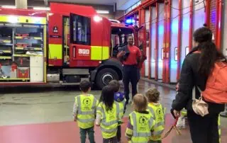 Firefighter demonstration at Monkey Puzzle Day Nurseries with young children in high-visibility vests learning safety skills.