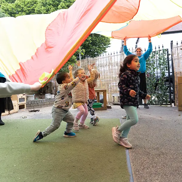 Nursery children enjoying parachute based outdoor activities with qualified nursery practitioners