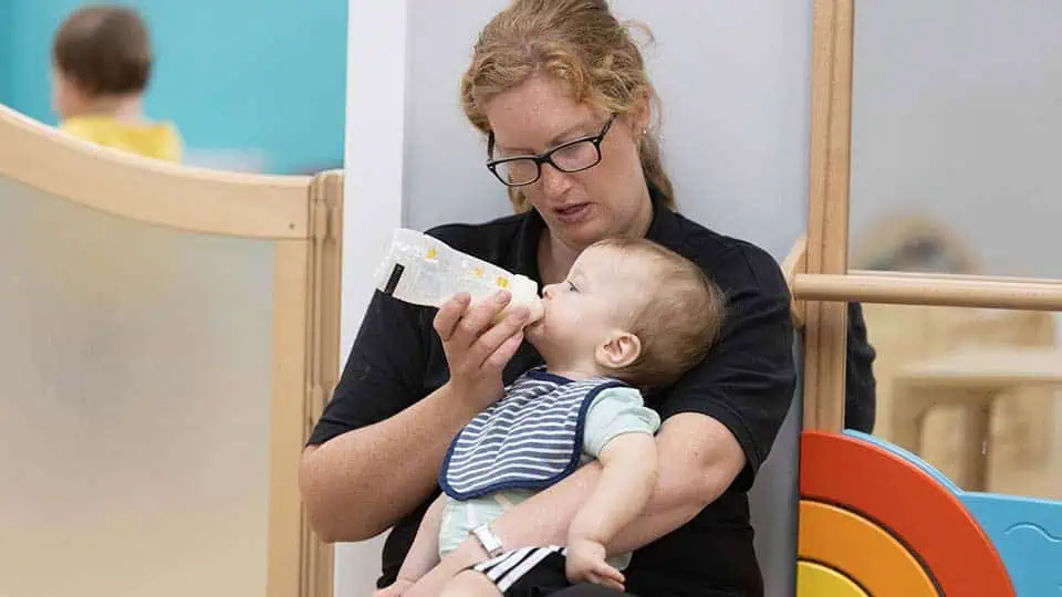 Staff bottle feeding a baby Bottle-feeding a baby in a childcare setting at Monkey Puzzle Day Nurseries, showcasing nurturing care and early childhood development.