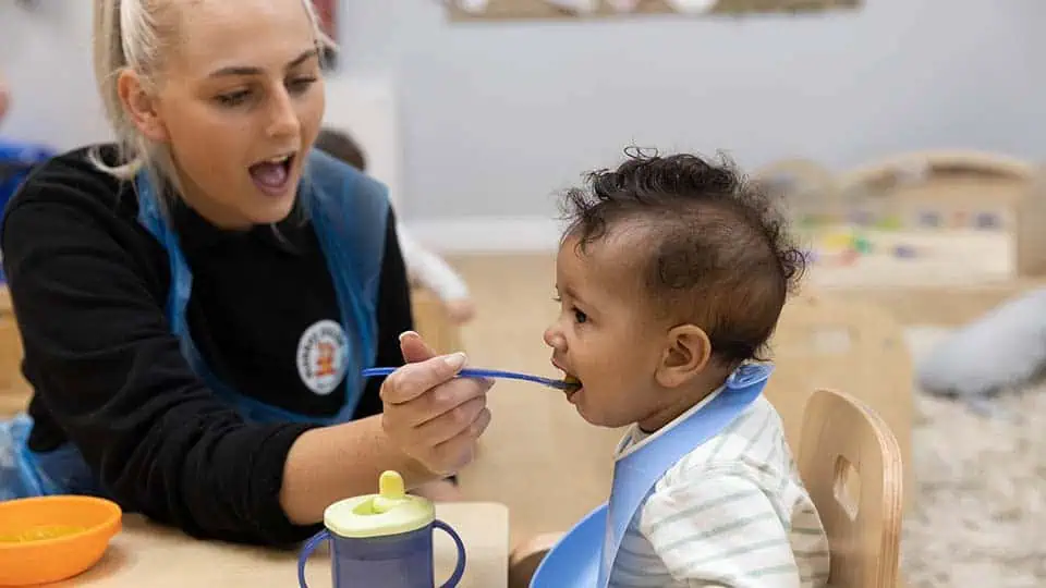 Lunch time at a Monkey Puzzle Nursery Delicious meal time with caring childcare professional feeding a young child at Monkey Puzzle Day Nurseries. The warm, nurturing environment promotes healthy eating habits for early childhood development.