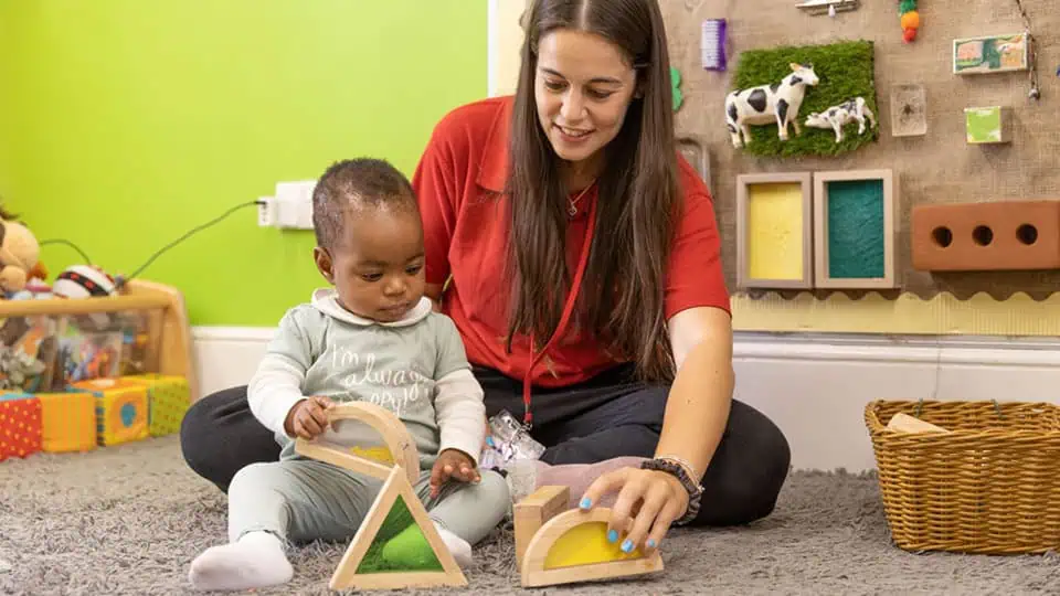 Staff and baby learning through play Colorful indoor nursery play area at Monkey Puzzle Day Nurseries with a caregiver engaging a young child in educational toys and activities.