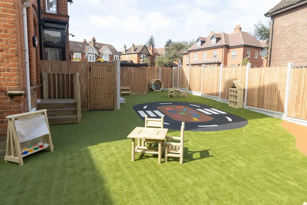 Outdoor space at a Monkey Puzzle Nursery Colorful outdoor play area at Monkey Puzzle Day Nurseries with artificial grass, wooden play equipment, and a hopscotch rug for early childhood development.