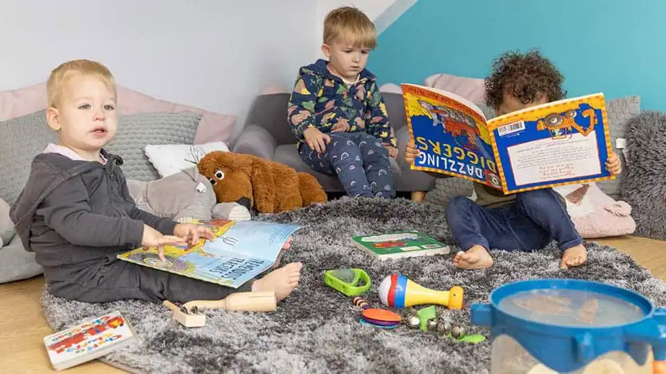 Toddler Reading Time Colorful young children engaging with picture books and toys in a bright nursery setting at Monkey Puzzle Day Nurseries.