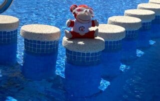 Colorful monkey plush toy wearing goggles, sitting on a circular flotation device, floating on the bright blue swimming pool at Monkey Puzzle Day Nurseries, representing fun and safety in early childhood swimming activities.