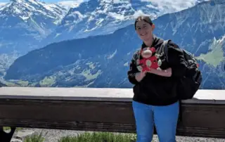 Mountains and a woman holding a camera at a scenic viewpoint in New Zealand.