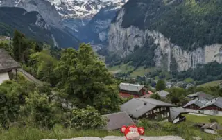 Cute monkey plush toy sitting on a rock with scenic Swiss Alps mountains in the background, representing child-friendly outdoor environments and natural beauty at Monkey Puzzle Day Nurseries.