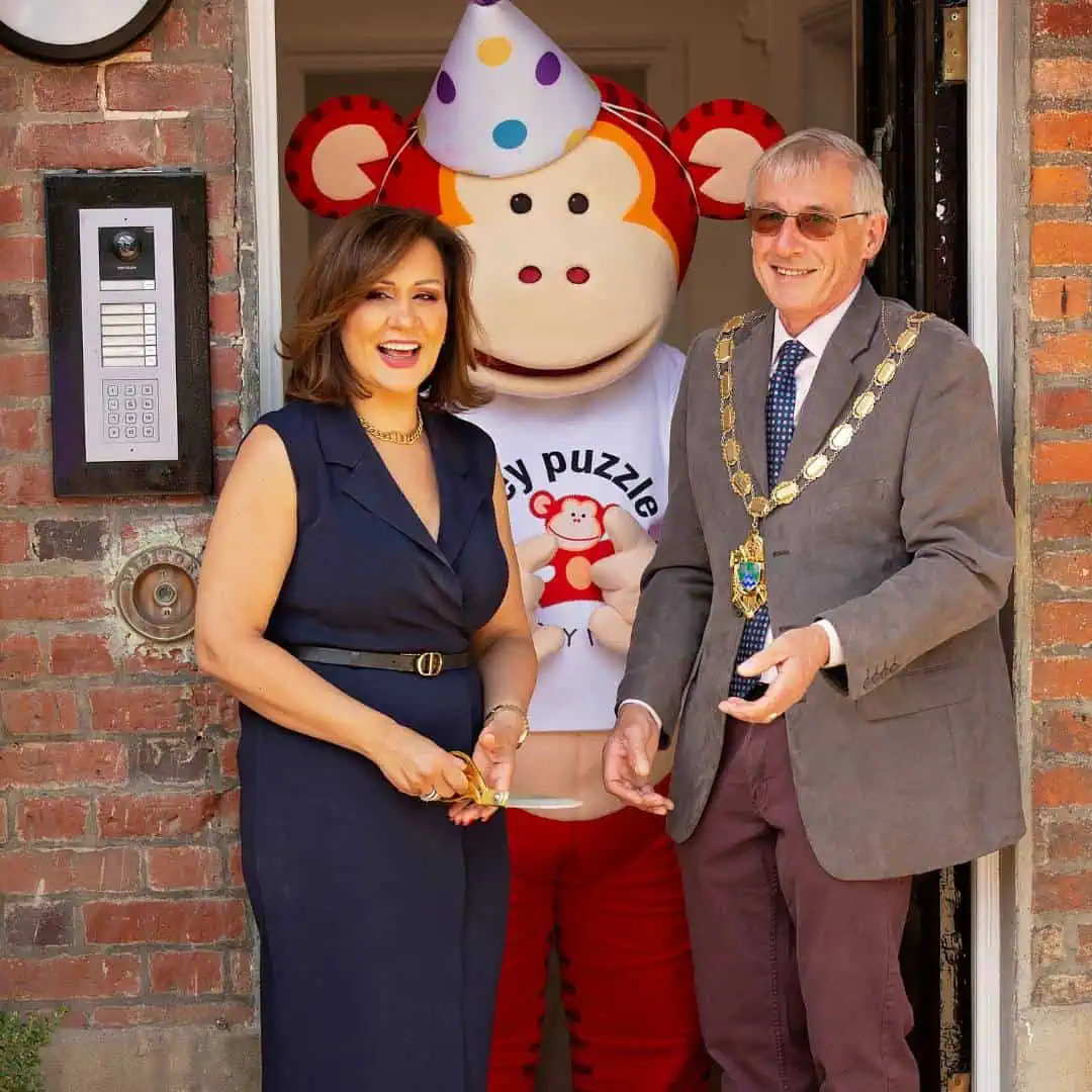 Large monkey puzzle mascot celebrating grand opening with woman and man in formal attire.