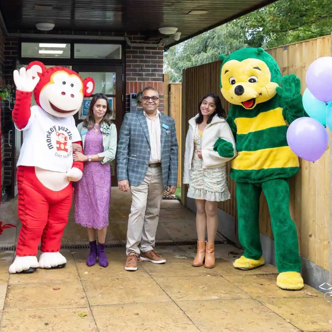 Colorful characters and staff celebrating at Monkey Puzzle Day Nurseries, outdoor event with kids' entertainers and balloons.
