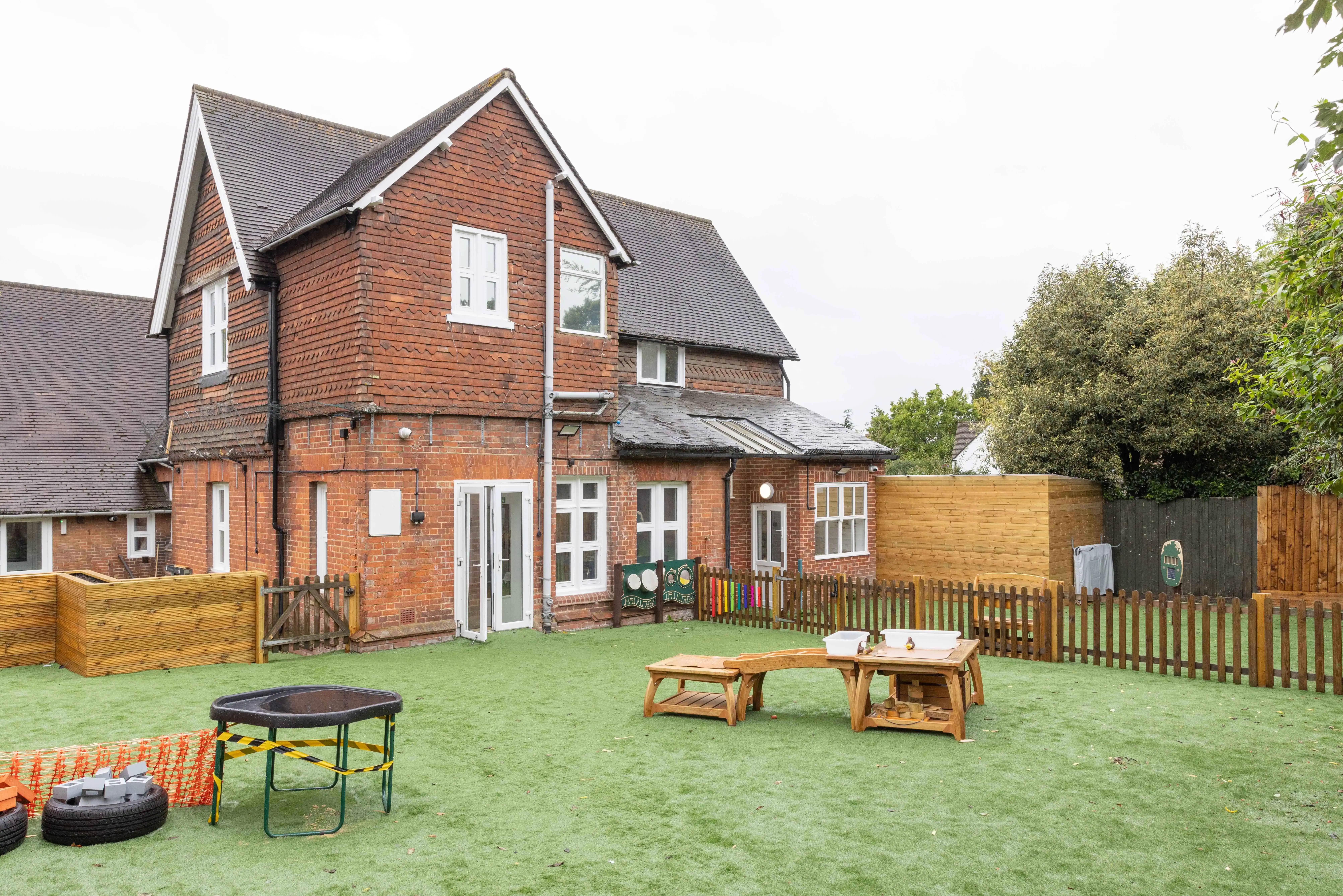 Bright outdoor playground at Monkey Puzzle Day Nurseries with artificial grass, wooden play structures, and fencing, providing a safe and engaging environment for children.