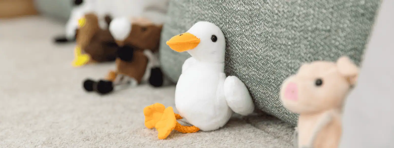 Soft plush toys including a white duck, pig, and brown dog displayed in a cozy childcare setting at Monkey Puzzle Day Nurseries.