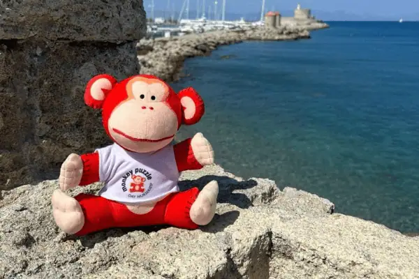 Monkey Puzzle Day Nurseries plush monkey toy sitting on rocks by the sea, promoting early childhood education, child care, and day nursery services in a scenic coastal setting.