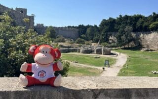 Monkey Puzzle Day Nurseries mascot plush toy sitting outdoors with a historic castle in the background.