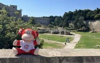 Monkey Puzzle Day Nurseries mascot plush toy sitting outdoors with a historic castle in the background.