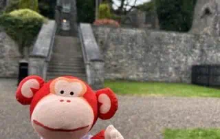 Colorful plush monkey toy in front of the historic castle steps at Monkey Puzzle Day Nurseries – fostering early childhood learning, play, and adventure in a nurturing environment.