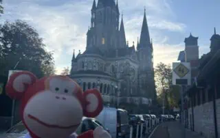 Colorful plush monkey toy in front of a historic church with tall spires during daytime.