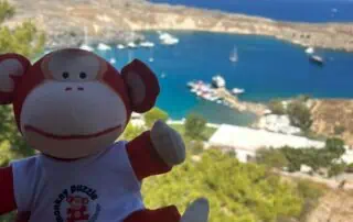 Colorful monkey plush toy with "Monkey Puzzle Day Nurseries" logo, scenic coastal view of boats and hills, perfect for children’s nursery branding and seaside adventure themes.