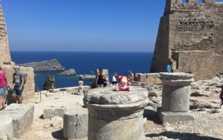 Ancient stone ruins overlooking the sea, with visitors exploring the historic site and the clear blue sky.