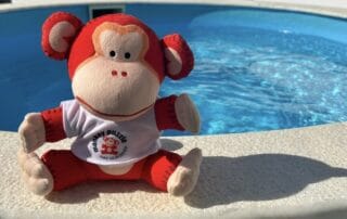 Soft toy monkey sitting on poolside at Monkey Puzzle Day Nurseries with a bright blue swimming pool in the background.
