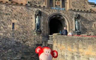 Colorful monkey plush toy in front of the historic Edinburgh Castle in Scotland, showcasing a fun and engaging atmosphere at Monkey Puzzle Day Nurseries for early childhood development.