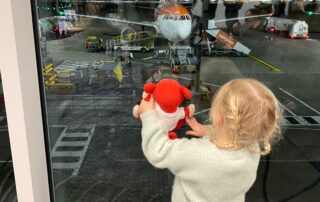 Child looking through airplane window at airport with teddy bear in hand, capturing the excitement of travel and exploration for early childhood development and adventure.