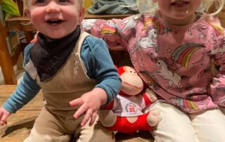 Cute toddlers at Monkey Puzzle Day Nurseries, smiling and playing together in a cozy indoor setting with toys and colorful decor.