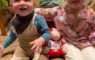 Cute toddlers at Monkey Puzzle Day Nurseries, smiling and playing together in a cozy indoor setting with toys and colorful decor.