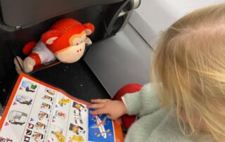 Learning activity with child reading a safety instruction booklet on an airplane seat safety, surrounded by child-friendly plush toys; perfect for early childhood safety education at Monkey Puzzle Day Nurseries.