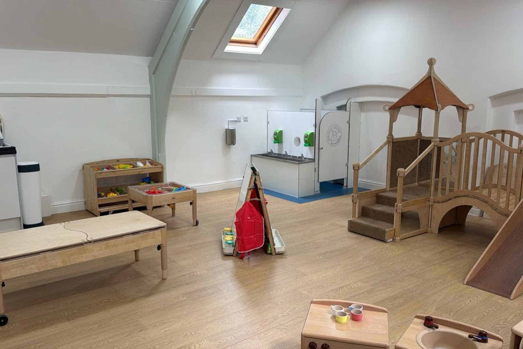 Bright and welcoming indoor play area at Monkey Puzzle Day Nurseries, featuring wooden toys, a slide, and a pretend kitchen, designed for early childhood development and safe, engaging learning experiences.