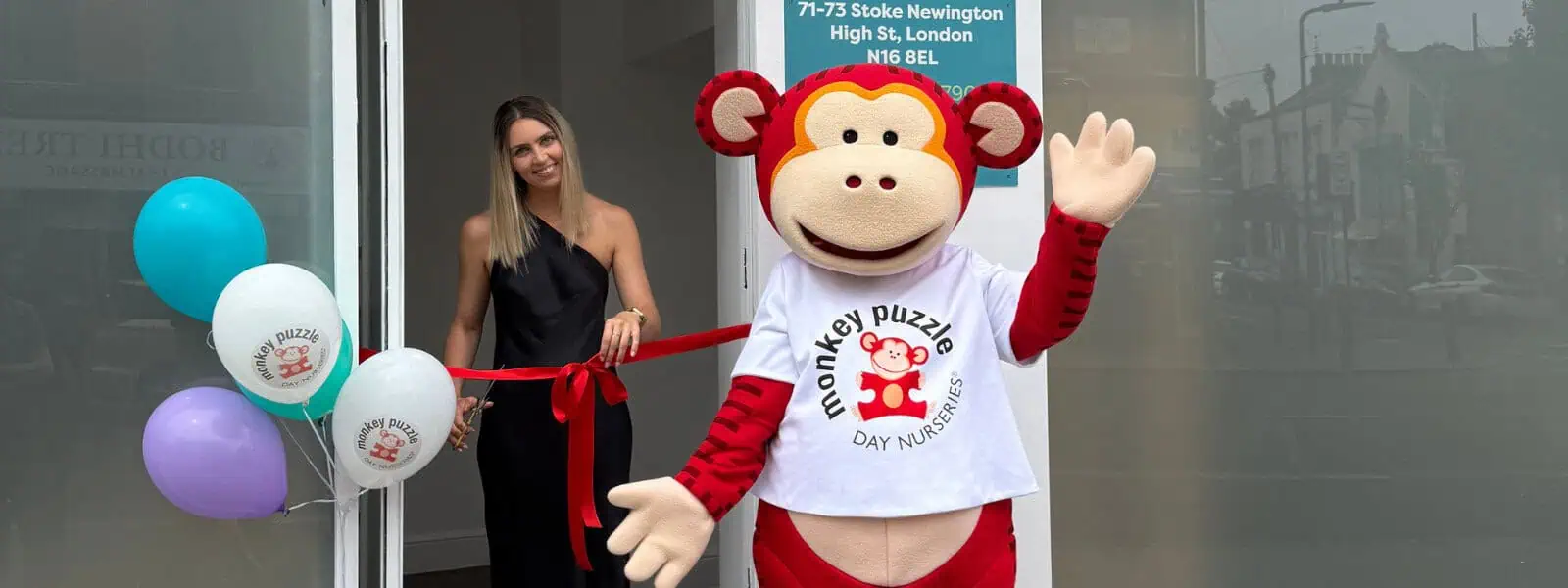 Colorful balloons and a cheerful woman with a monkey mascot celebrating the opening of Monkey Puzzle Day Nurseries in London at 71-73 Stoke Newington High St.