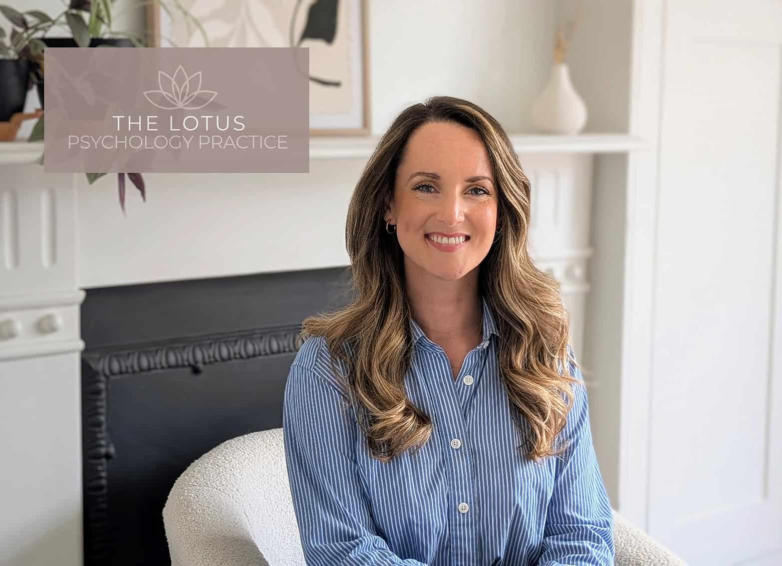 The Lotus Psychology Practice Team A professional woman with long wavy hair smiling in a cozy, well-lit office environment, representing The Lotus Psychology Practice.