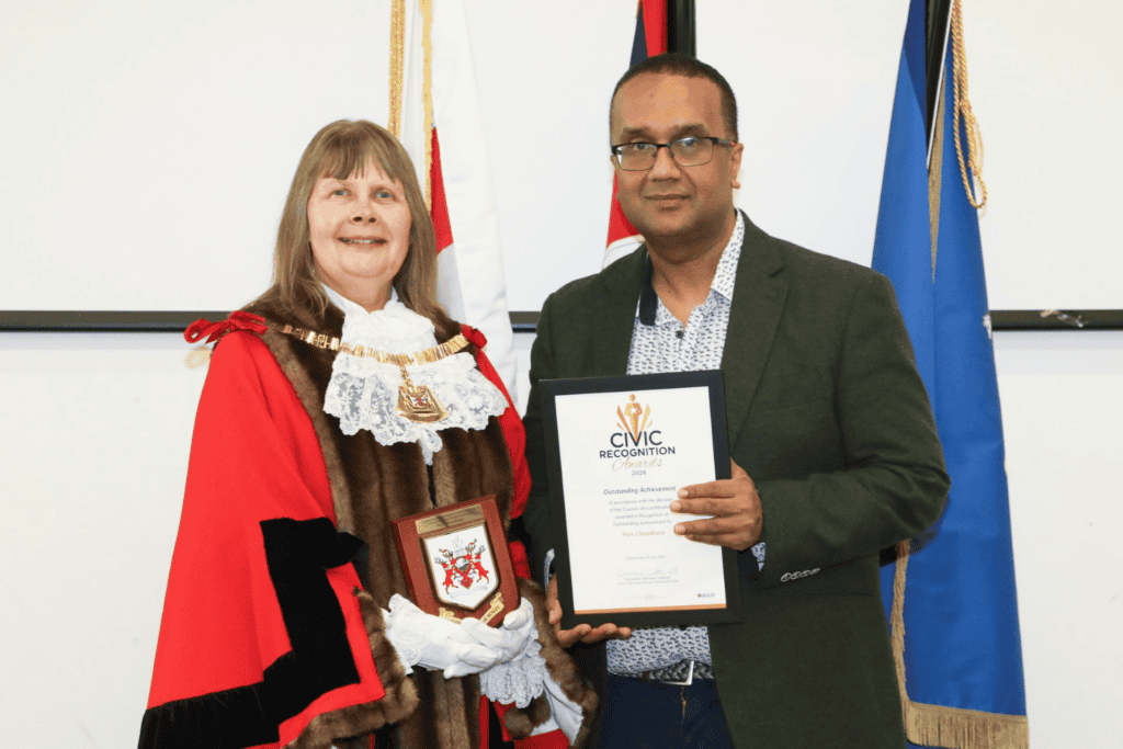 A woman in ceremonial robes and a man holding a civic recognition certificate at Monkey Puzzle Day Nurseries event.