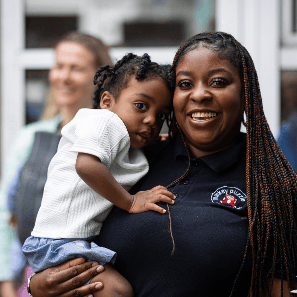 Happy Child and Caregiver at Day Nursery Smiling caregiver holding a happy young girl at Monkey Puzzle Day Nurseries, showcasing caring environment for children's emotional development.