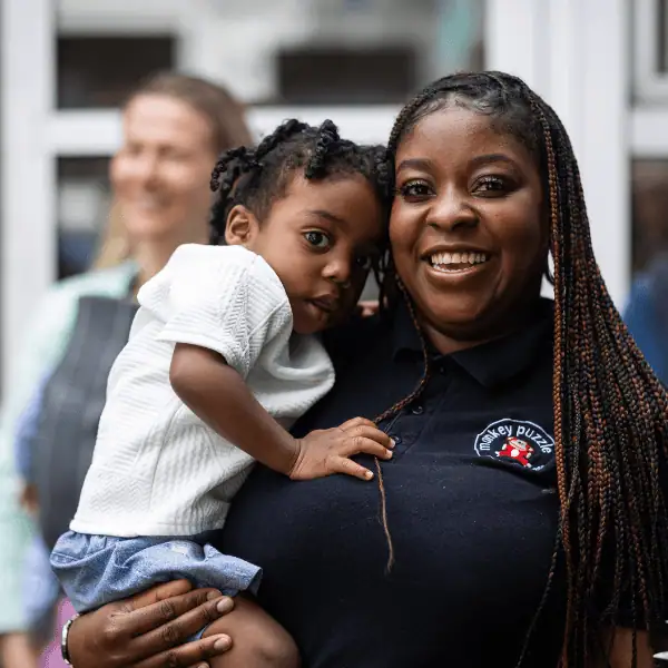 Happy Child and Caregiver at Day Nursery Smiling caregiver holding a happy young girl at Monkey Puzzle Day Nurseries, showcasing caring environment for children's emotional development.