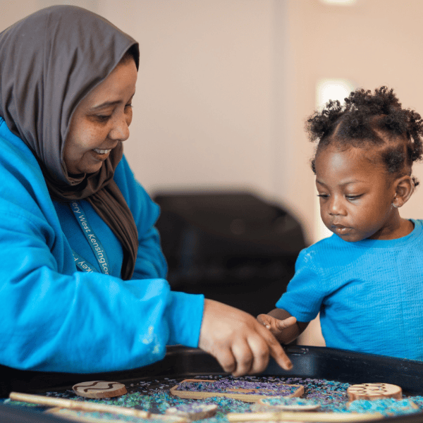 Child and Caregiver Engaged in Play A caregiver and young child playing with decorated cookies at a daycare, fostering learning and social skills.